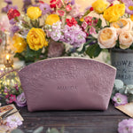 Personalized leather makeup bag with an all-over floral emboss in lilac, name Amanda, set among bright blooms