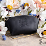Black leather makeup bag with a floral monogram deboss on a gold tray with spring blooms