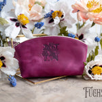 Fuchsia leather makeup pouch with an ornate monogram deboss on a gold tray with blooms