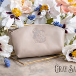 Gray sand leather makeup pouch with a floral monogram deboss, styled on a gold tray with fresh flowers