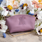 Lilac leather makeup pouch with a floral monogram deboss, styled with fresh blooms