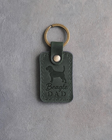 Forest green leather keychain debossed with a Beagle silhouette and the words Beagle DAD, on gray concrete