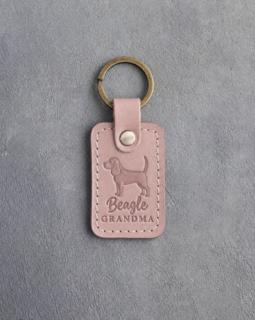 Blush pink leather keychain debossed with a beagle silhouette and the words Beagle GRANDMA, on gray concrete