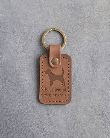 Caramel leather keychain debossed with a Beagle silhouette above Best friend and THE BEAGLE, on gray concrete
