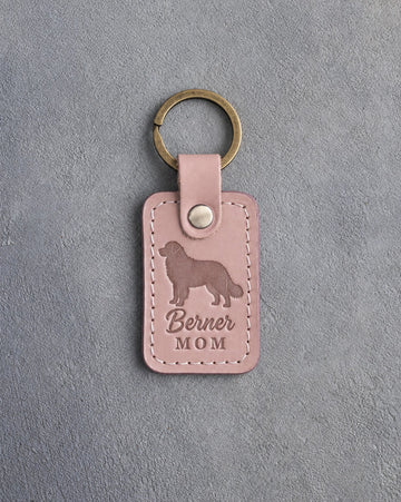 Blush pink leather keychain debossed with a Bernese mountain dog silhouette and the words Berner MOM, on gray concrete