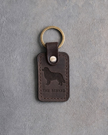 Dark espresso leather keychain debossed with a Bernese mountain dog above THE BERNER, on gray concrete