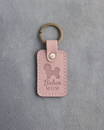 Blush pink leather keychain with a debossed Bichon Frise and the words Bichon MOM on gray concrete