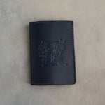 Black leather passport cover with a large floral initial pressed into the front
