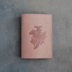 Blush leather passport cover with a large floral initial J pressed into the front