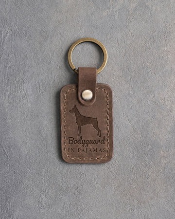 Sicilian brown leather keychain debossed with a Doberman silhouette and the words Bodyguard IN PAJAMAS, on gray concrete
