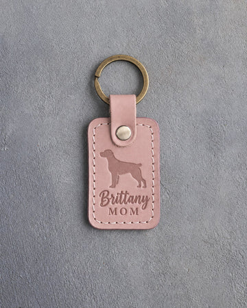 Blush pink leather keychain debossed with a Brittany silhouette and the words Brittany MOM, on gray concrete