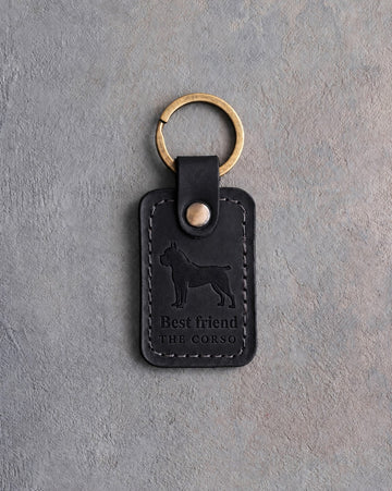 Black leather keychain debossed with a Cane Corso above Best friend and THE CORSO, on gray concrete