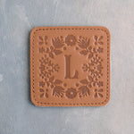 Caramel leather coaster with the floral frame and an initial pressed in