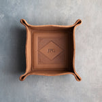 Caramel leather valet tray with snapped corners and the initials JPG pressed into the diamond frame, seen from above