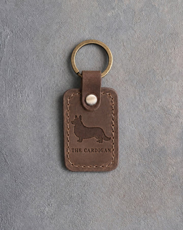 Sicilian brown leather keychain debossed with a Cardigan Welsh Corgi silhouette above THE CARDIGAN, on gray concrete