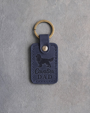 Blueberry navy leather keychain debossed with a Cavalier King Charles Spaniel silhouette and the words Cavalier DAD, on gray concrete