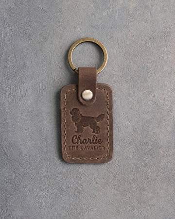 Sicilian brown leather keychain debossed with a Cavalier King Charles Spaniel silhouette, the name Charlie and THE CAVALIER, on gray concrete