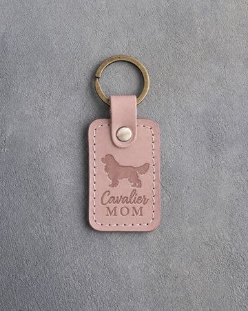 Blush pink leather keychain debossed with a Cavalier King Charles Spaniel silhouette and the words Cavalier MOM, on gray concrete