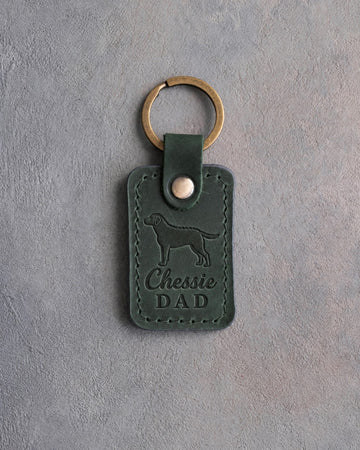 Forest green leather keychain debossed with a Chesapeake Bay retriever and Chessie DAD lettering, on gray concrete
