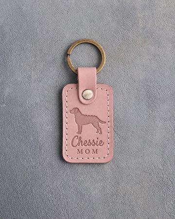 Blush pink leather keychain debossed with a Chesapeake Bay retriever and the words Chessie MOM, on gray concrete