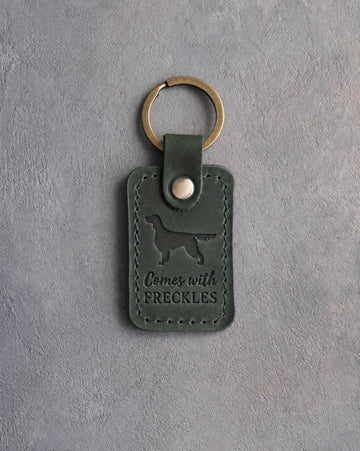 Forest green leather keychain debossed with an English Setter silhouette and the words Comes with FRECKLES, on gray concrete