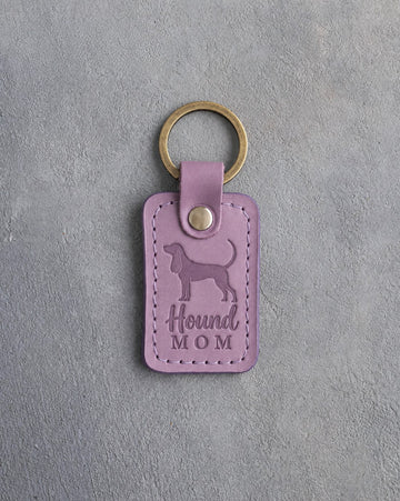 Lilac leather keychain debossed with a Coonhound silhouette and the words Hound MOM, on gray concrete