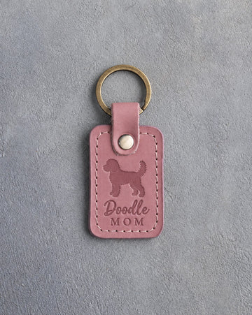 Parisian Blossom pink leather keychain with a debossed goldendoodle and the words Doodle MOM on gray concrete
