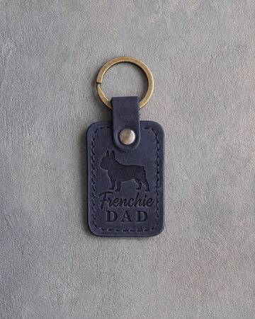 Blueberry navy leather keychain with a debossed French bulldog and Frenchie DAD lettering, on gray concrete