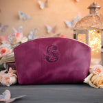 Fuchsia initial makeup pouch with a floral monogram, staged among pale roses on a slate table