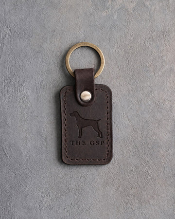 Dark espresso leather keychain debossed with a German Shorthaired Pointer silhouette above THE GSP, on gray concrete