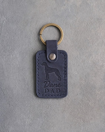 Blueberry navy leather keychain debossed with a Great Dane silhouette and Dane DAD, on gray concrete