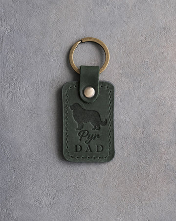 Forest green leather keychain debossed with a Great Pyrenees silhouette and Pyr DAD on gray concrete