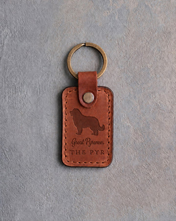 Arizona tan leather keychain debossed with a Great Pyrenees above Great Pyrenees and THE PYR, on gray concrete