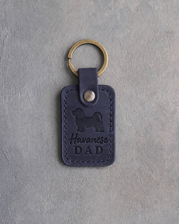 Blueberry navy leather keychain debossed with a Havanese silhouette and Havanese DAD, on gray concrete
