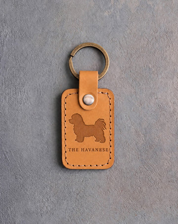Indian Summer tan leather keychain debossed with a Havanese above THE HAVANESE, on gray concrete