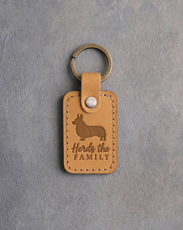 Indian Summer tan leather keychain debossed with a corgi silhouette and the words Herds the FAMILY, on gray concrete
