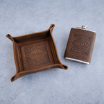 Valet tray and flask gift set: a brown leather valet tray and a leather hip flask, both stamped DAD in a diamond frame