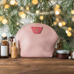 Blush round leather makeup bag with skincare bottles under a softly lit tree