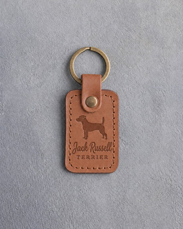 Caramel leather keychain debossed with a Jack Russell terrier above Jack Russell and TERRIER, on gray concrete