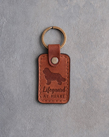 Arizona tan leather keychain debossed with a Newfoundland and the words Lifeguard AT HEART, on gray concrete
