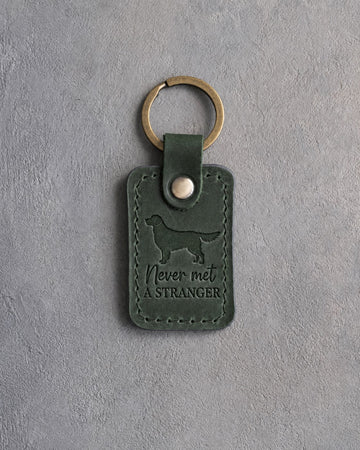 Forest green leather keychain with a debossed golden retriever and the phrase Never met A STRANGER on gray concrete