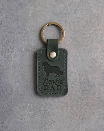 Forest green leather keychain debossed with a Newfoundland silhouette and Newfie DAD on gray concrete