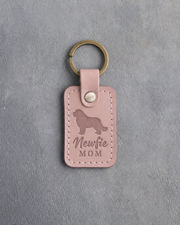 Blush pink leather keychain with a debossed Newfoundland and the words Newfie MOM, on gray concrete