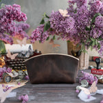 Dark espresso leather makeup pouch with a gold name, lilacs and vintage props around
