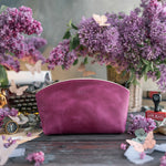 Personalized leather makeup bag in orchid fuchsia with a small monogram, styled among lilac blooms