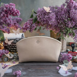 Cream leather makeup pouch with a gold floral emblem, styled among lilacs