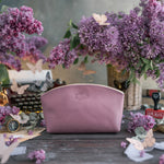 Lilac leather makeup pouch with a delicate gold monogram, matching purple lilacs behind