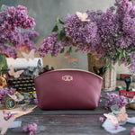 Sangria burgundy leather makeup pouch with a cursive gold monogram, lilac blooms around