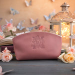Dusty pink leather makeup bag with a floral letter M, framed by pale roses