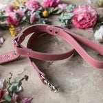 Personalized pink leather dog leash with a cursive name tab among flowers